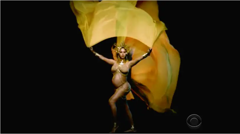 Beyonce in her Grammys 2017 performance, visibly pregnant in a golden crown with flowing golden fabric behind her